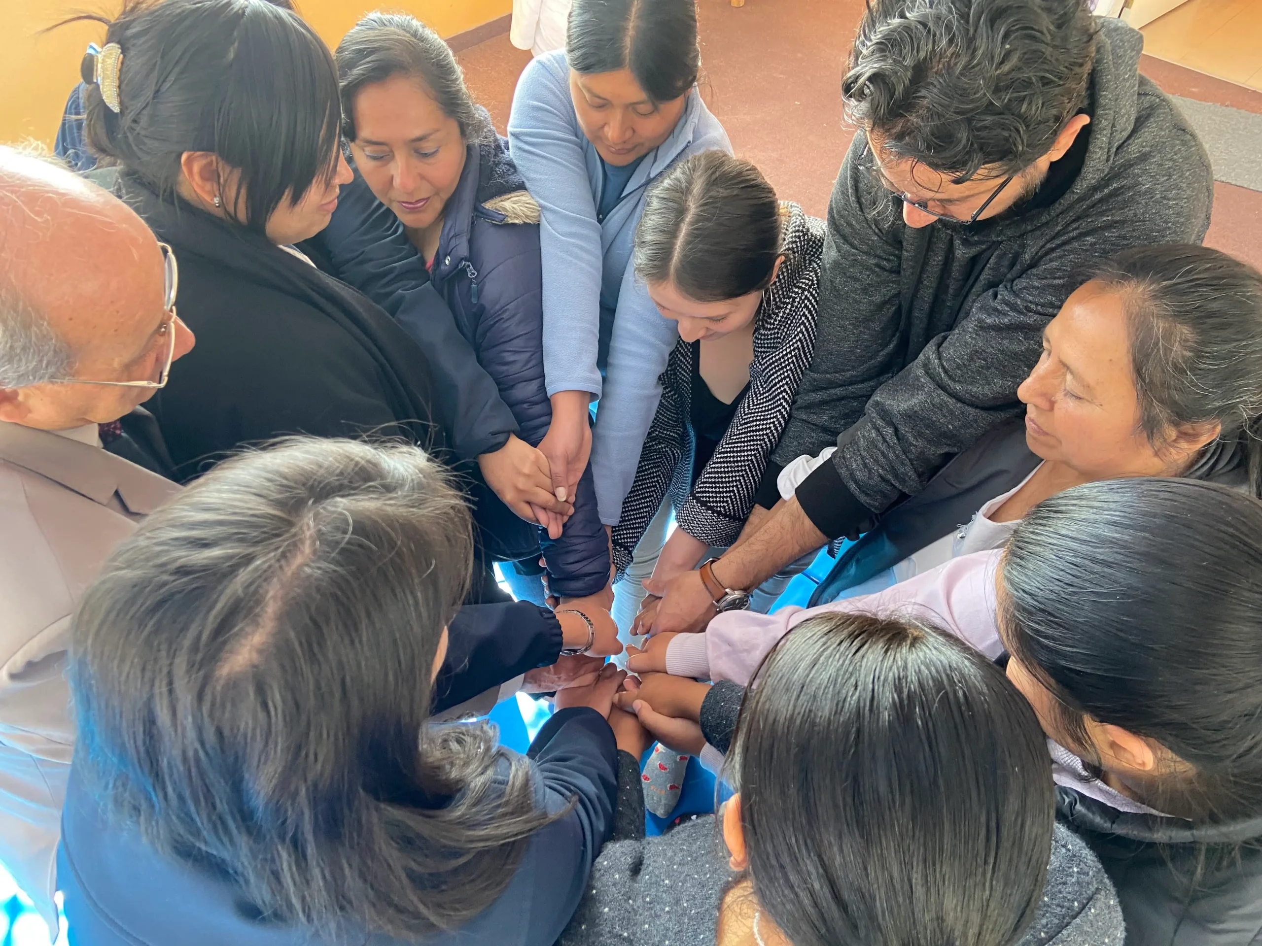 Grupo de personas formando un círculo y uniendo sus manos al centro como gesto de compromiso y solidaridad comunitaria.