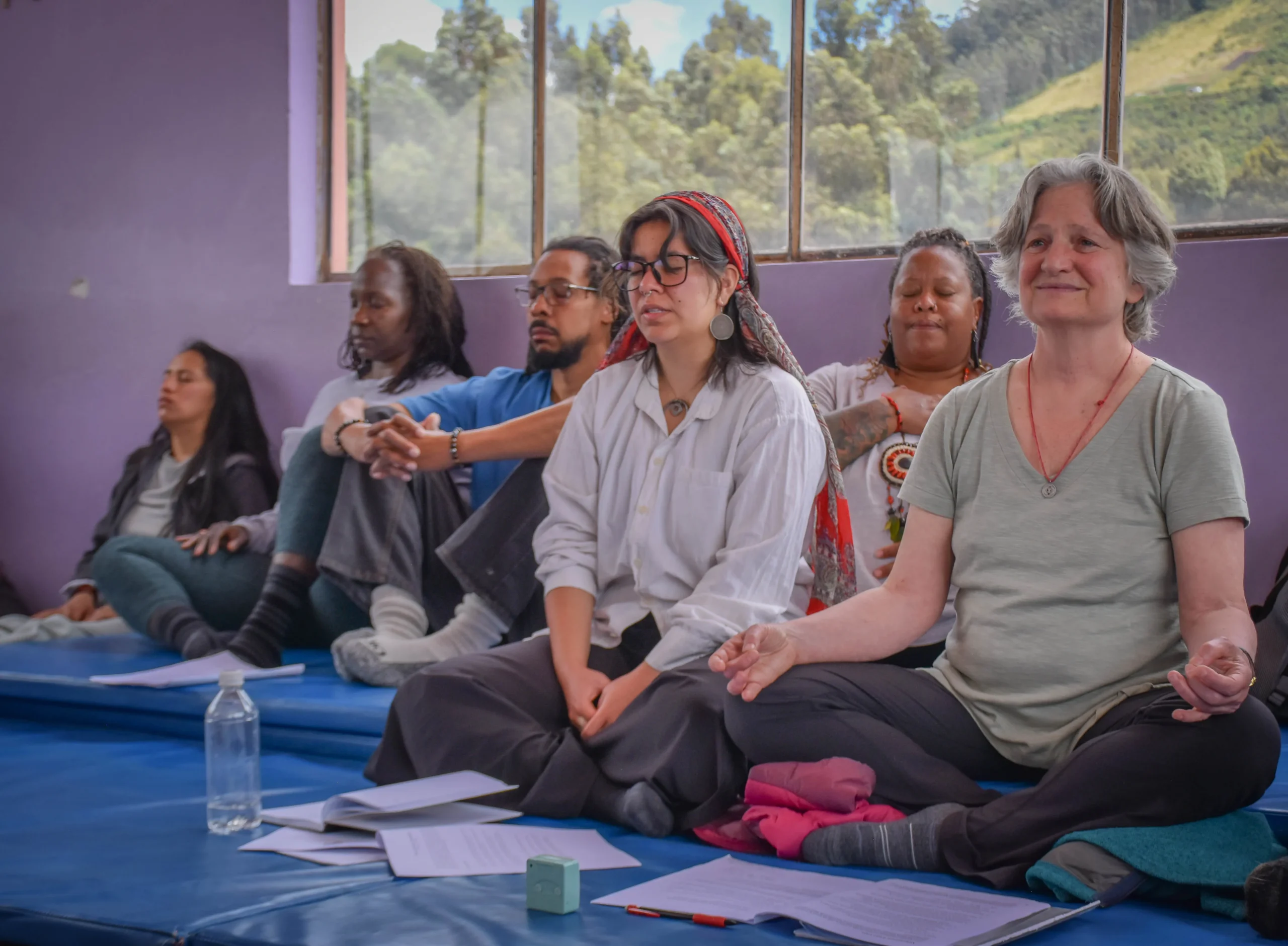 Grupo de personas sentadas en colchonetas realizando una práctica de meditación en un ambiente comunitario que refleja diversidad y respeto.