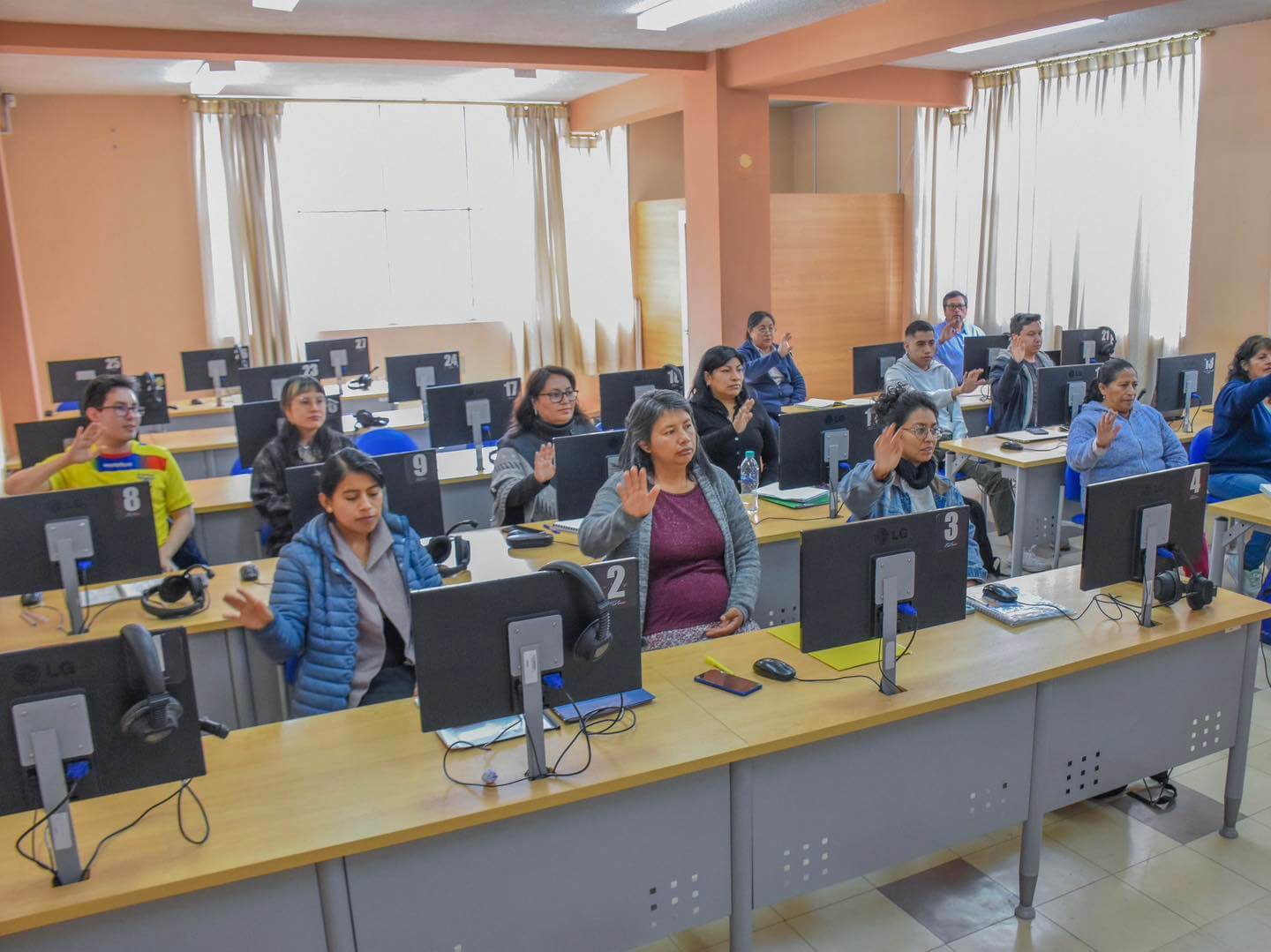 Grupo de docentes del INEPE levantando la mano en un aula de informática durante una sesión de capacitación en tecnología educativa y herramientas digitales.