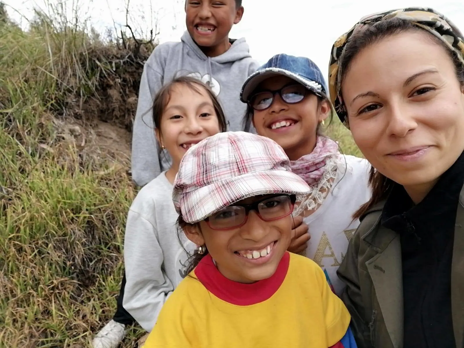 Una mujer joven y cuatro niños sonrientes posan para una fotografía en un entorno natural al aire libre durante una jornada de educación popular.